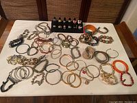 48 assorted bracelets including metal bangles, beaded bracelets, stretch bands, and charm bracelets spread on a table.