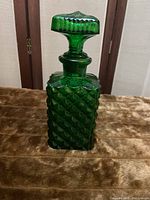 Front view of vintage green diamond cut glass decanter with stopper on a brown surface.
