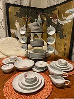 Overall view of the 55 piece Gildhar LTD Fine Porcelain Petite Rose dish set displayed with metal stand and arranged on table.