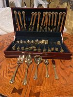 Photo showing entire set arranged inside polished wood chest with slots and dark blue felt lining, utensils are gold plated with ornate American Chippendale floral and scrollwork design handles.