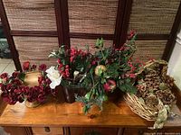 Overview of four seasonal floral arrangements on wooden surface, shows variety of items including red flowers, pinecones, berries, and gold accents