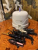 Photo showing Gold N Hot 1200 hood hair dryer with coiled cords from multiple curling irons and flat irons arranged in front.