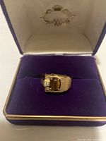 Men's 14K gold ring with brown oval stone and small clear stone in purple velvet ring box, top angled view.