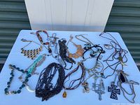 Full view of all assorted costume necklaces arranged on white surface showing variety of styles, lengths, colors including chains, beads, and pendants.