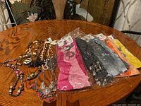 Wide angled view of the five costume necklaces laid out on a table and five individually wrapped jewelry scarves in different colors.