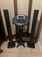 Front view of Singing Machine Classic karaoke machine flanked by two tall Philips speakers on either side, placed on tile floor.