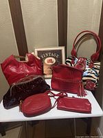 Six assorted red and animal print ladies' purses and pouches arranged on a white surface with a vintage sign behind.