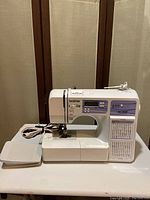 Full view of Brother HC1850 sewing machine with attached power cord and foot pedal on table.