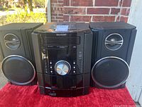 Front view of stereo system showing main unit between two speakers with visible volume knob and speaker cones.
