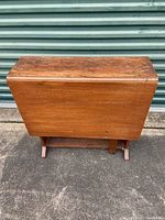 Wood folding drop-leaf table in folded position showing wood grain and wear on top surface.