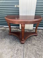 Front view of cherry wood half-moon entry table showing carved legs and lower shelf, surface has scratches.