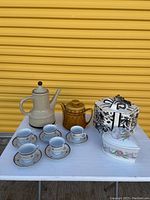 Overview of the complete set showing two teapots, five tea cups and saucers, and two ceramic boxes on white table against yellow background.