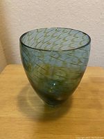 Angled side view of a blue and green glass vase showing its rounded shape and swirl pattern.