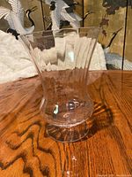 Clear glass vase with flared scalloped shape and pedestal base on wooden surface