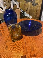Photo showing all three items together: blue vase, blue bowl, amber gold vase on wooden table