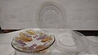 Three glass plates, two clear with ribbed circular designs and one decorative with painted grapes and leaves.