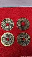 Four Chinese copper coins displayed on a red surface, showing front side with Chinese inscriptions and square center holes.