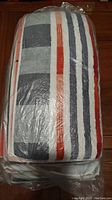 Photo of unopened packages of colorful striped cotton towel showing towel folded with visible serial stripes of grey, white, red, orange and black on plastic wrapping.