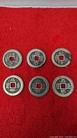 6 Chinese copper coins arranged in two rows of three on red fabric background, showing Chinese characters around the central square hole.