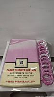Photo of packaged fabric shower curtain with water repellent label and 12 fabric covered rings.