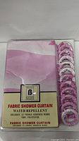 Packaged fabric shower curtain with label showing water repellent feature and included 12 fabric covered rings.