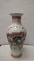 Front view of Chinese porcelain vase depicting children playing under trees and floral motifs with red decorative borders on neck and base.