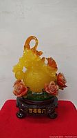 Front view of yellow translucent double gourd figurine decorated with floral accents on dark wooden stand.
