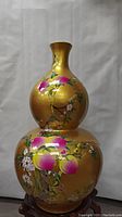 Front view of a large golden double gourd shaped bottle with hand-painted pink and yellow fruit and white floral branches.
