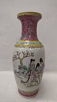 Side view of the porcelain vase showing hand painted Chinese women near a blossoming tree with floral patterned neck and rim.