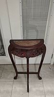 Front angle of wooden side table with semi-circular brown marble top and carved apron detailing on three cabriole legs.