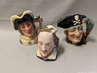 Three character mugs shown together featuring British soldier, Shakespeare, and pirate with parrot