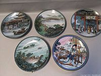 Top view showing all five plates with various Asian scenes: boats, pagoda, river, bridge, and figures indoors.