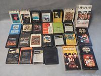 Overview of lot showing a variety of 8 track tapes and VCR tapes laid out flat on a surface, arranged in rows