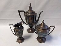Photo of three-piece Art Deco silver plated tea set showing teapot, creamer, sugar bowl with lids and handles.