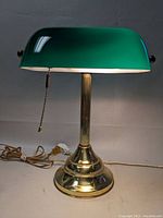 Front angled view of banker desk lamp with visible brass base, green glass shade, pull chain, and power cord.