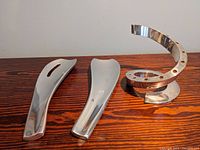 Photo showing two stainless steel kitchen utensils and one spiral stainless steel candle holder on wooden surface.