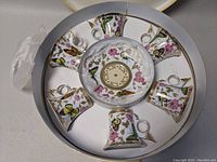 Top-down view of 6 demitasse cups and 6 saucers arranged inside a round box, showing detailed butterfly and flower decorative patterns with gold trim.