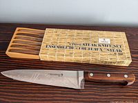 6-piece Henckles steak knife set shown inside wooden storage case with one knife displayed in front.