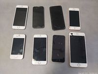 Top view of 8 iPhones showing front facing screen condition, some cracked or damaged