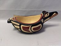 Side view of the wooden bird-shaped bowl showing detailed Haida painted design and bird profile.