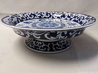 Side angle view showing the height and detailed scrolling patterns on the rim and pedestal base.