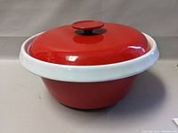 Front angle view of red enamel pot with white rim and lid with knob.