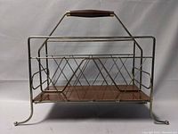 Front view of mid-century modern style magazine holder with metal wire frame, wooden handle, and base.