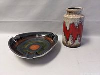 Two pieces of West German pottery displayed, a triangular decorative plate with circular patterns and a cylindrical vase with red zigzag design