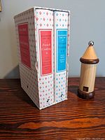 Two hardcover volumes of 'Mastering The Art of French Cooking' by Julia Child in decorative slipcase and a Peugeot pepper grinder on wood table.