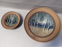 Two oval stoneware bowls, large and small, both featuring a birch tree painting inside with speckled tan exterior.