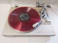 Top view of turntable playing a red vinyl record (not included), showing metal plinth and tonearm.