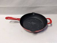 Front and angled view of red cast iron enamel skillet showing interior cooking surface and handles.