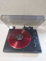 Sony PS-LX230 vintage turntable with clear dust cover open showing red translucent vinyl record on platter, front view.