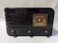 Front view of Stromberg-Carlson tube radio showing black Bakelite case, horizontal ridged details, tuning dial with frequency markings and three control knobs.